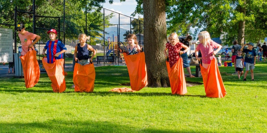 Six smiling children participating in a sack race on a sunny day.